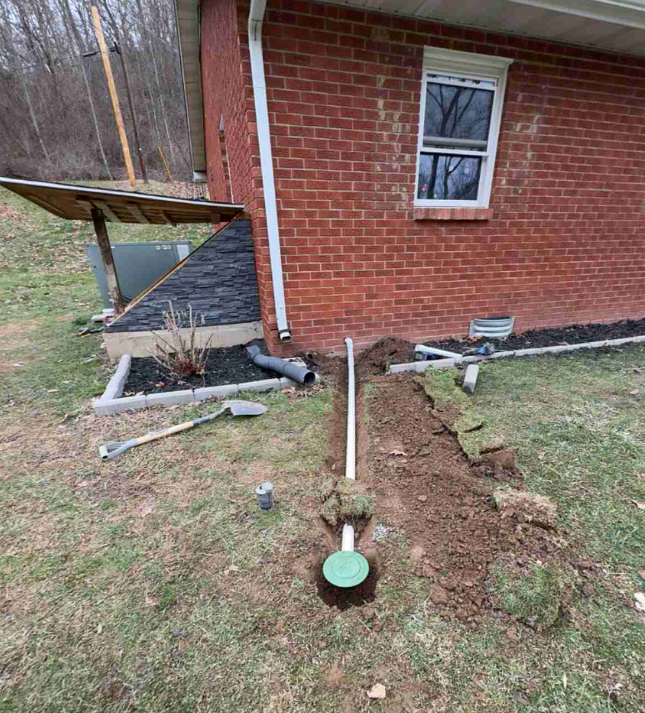 Exterior basement waterproofing work in Lexington KY showing a trench dug beside a brick home with newly installed drainage piping and soil removed for proper water diversion.