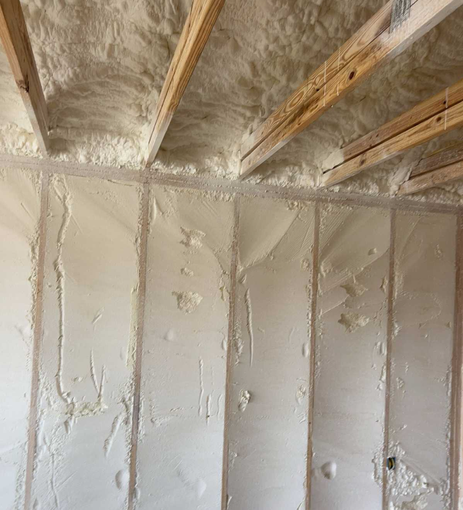 Spray foam insulation applied to wall cavities and ceiling joists inside a partially finished room.