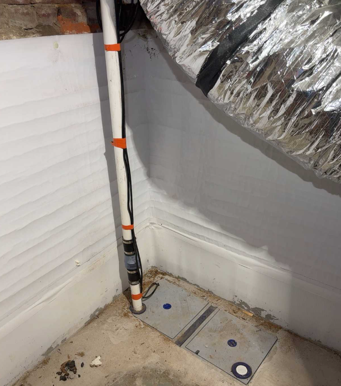 A newly installed sump pump discharge line in a Lexington KY basement, showing PVC piping, drainage covers, and moisture‑barrier wall panels as part of a waterproofing system.