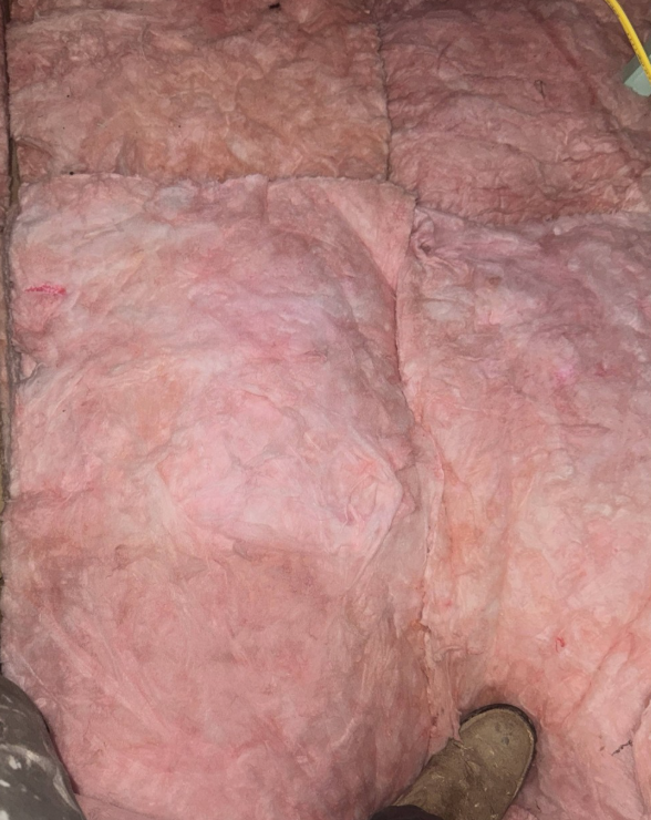 Pink fiberglass batt insulation covering an attic floor with a boot partially visible in the lower corner.