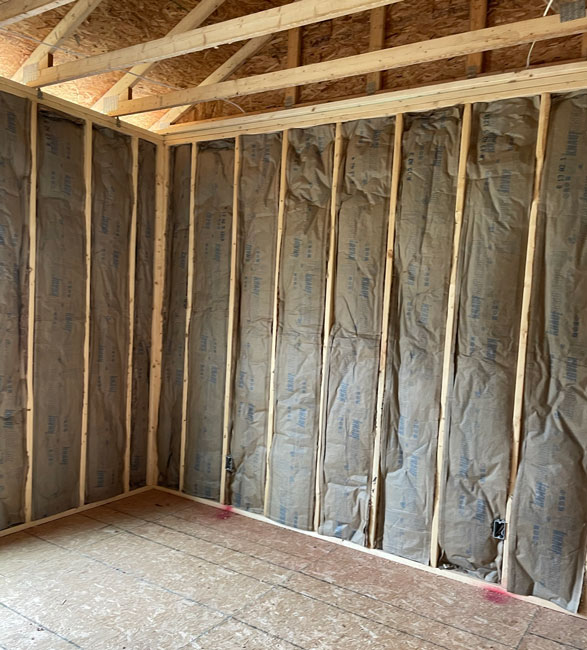 Faced fiberglass batt insulation installed between vertical wooden wall studs inside a newly framed room beneath exposed ceiling trusses.