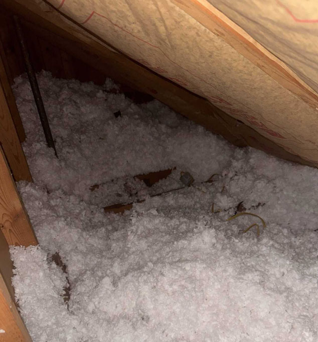 An attic space filled with thick, white loose-fill blown-in insulation across the floor, with paper-faced insulation batts installed along the sloped roof rafters.