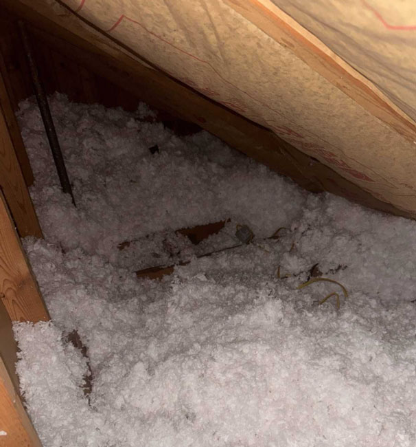 Thick white blown-in loose-fill insulation spread across an attic floor under kraft-faced fiberglass roof rafter batts.