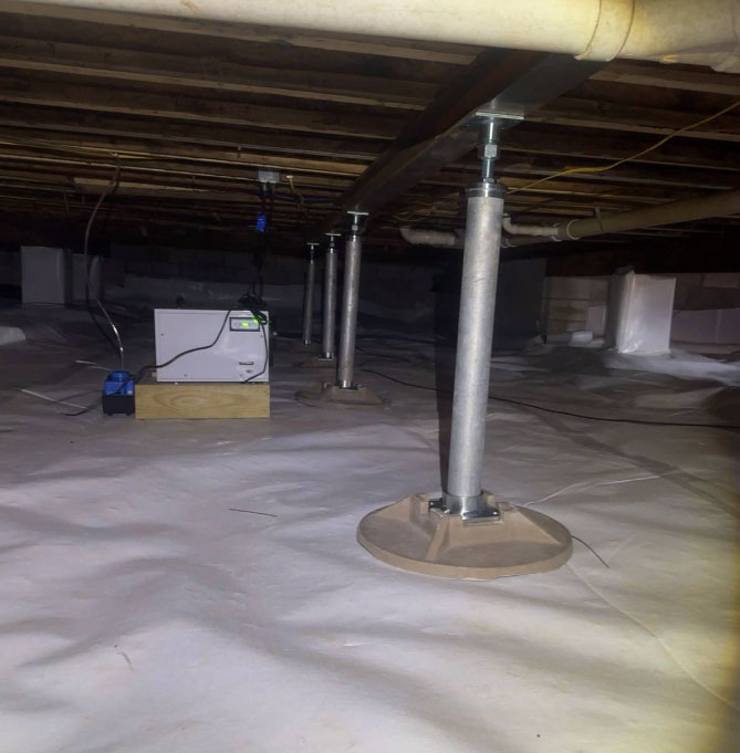An encapsulated crawl space with a white plastic vapor barrier lining the floor, featuring adjustable metal jack posts supporting a steel main beam and a commercial dehumidifier running in the background.