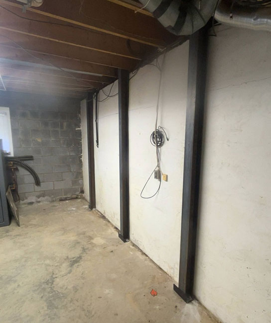 Heavy-duty steel I-beams installed vertically against a painted basement wall to reinforce and stabilize a bowing foundation wall.