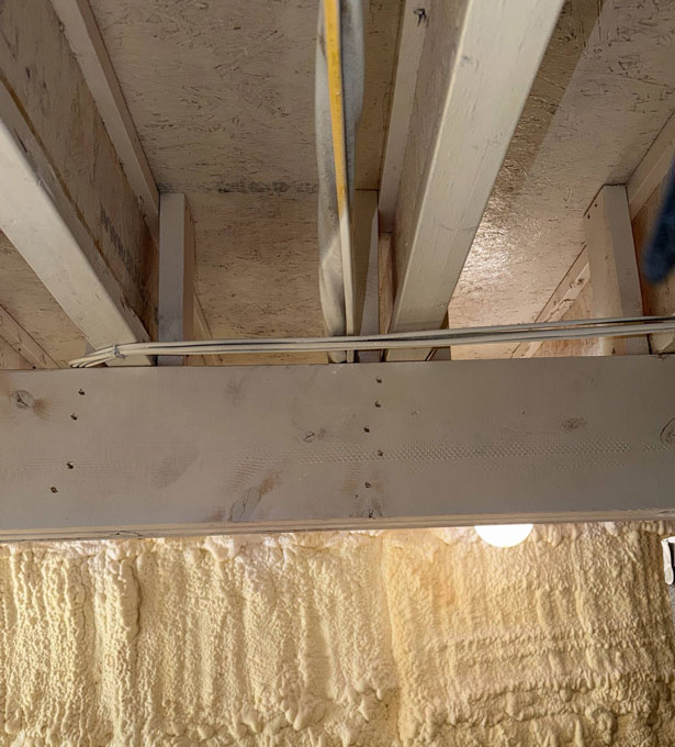 Clean engineered I-joists and subfloor framing sealed above wall spray foam insulation in a basement or crawl space.