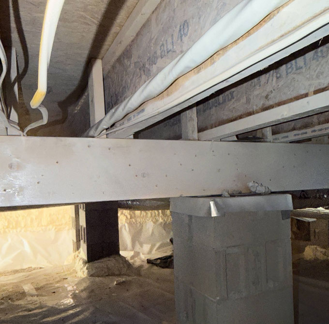 Clean, treated wooden support beam resting on concrete block piers in a fully encapsulated crawl space with a bright white vapor barrier.