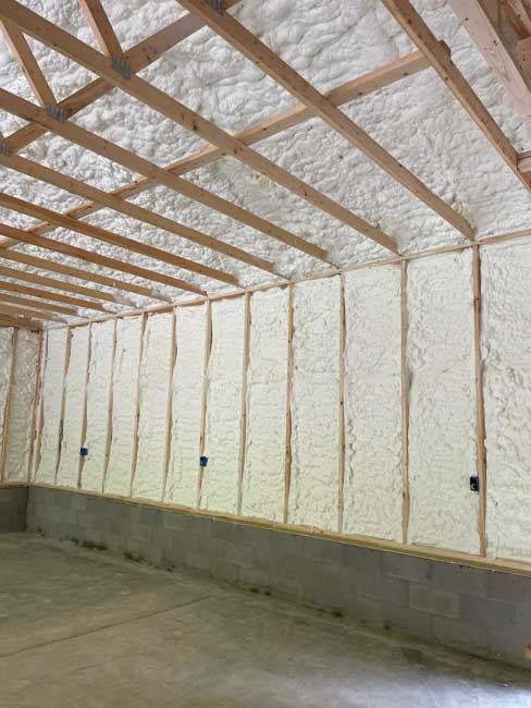 Bright white spray foam insulation completely coating the wall cavities and vaulted ceiling roofline above a concrete block foundation wall in a new building structure.