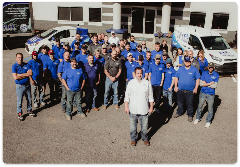 The Reed's Home Solutions team posing together in matching blue shirts outside their office building alongside company service vehicles in Roanoke.