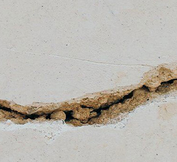 A detailed close-up of a wide horizontal crack with exposed crumbling concrete running through a light gray foundation wall.