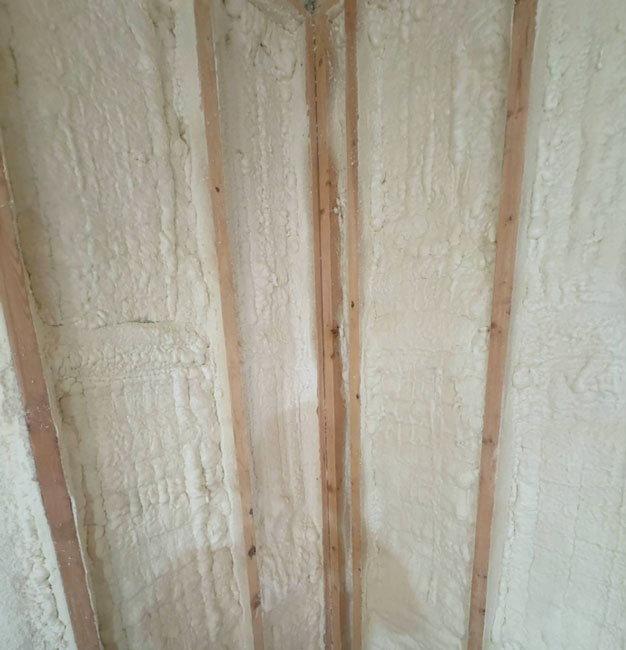Thick white spray foam insulation completely filling wooden wall stud cavities at an interior corner.